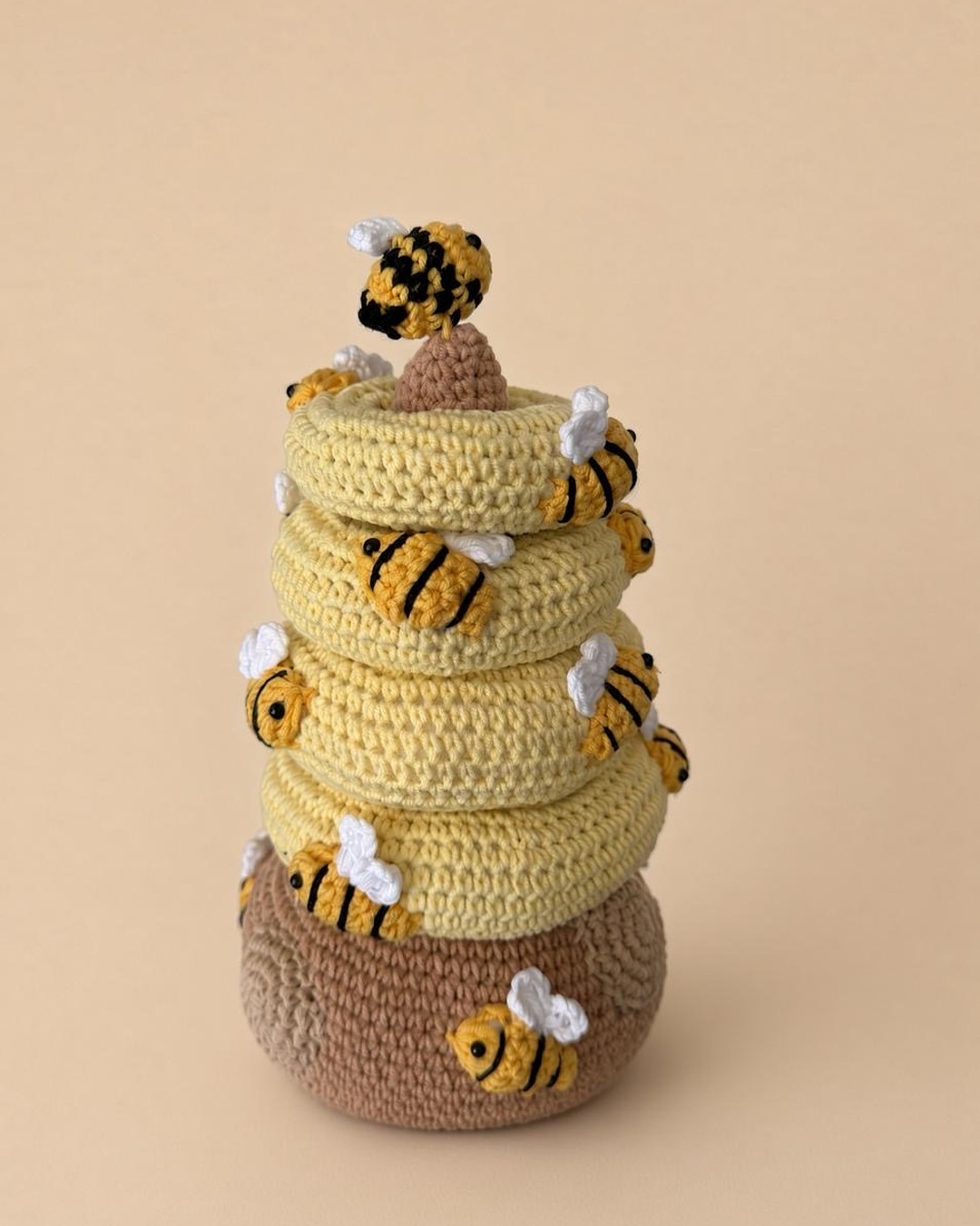 Handmade crochet beehive stacker with a brown base, four yellow rings, a brown top and little striped bees