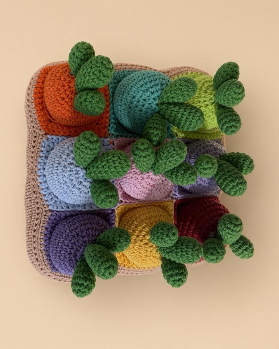 Handmade crochet carrot garden seen from above: nine colourful carrots with green tops planted in a soft garden bed