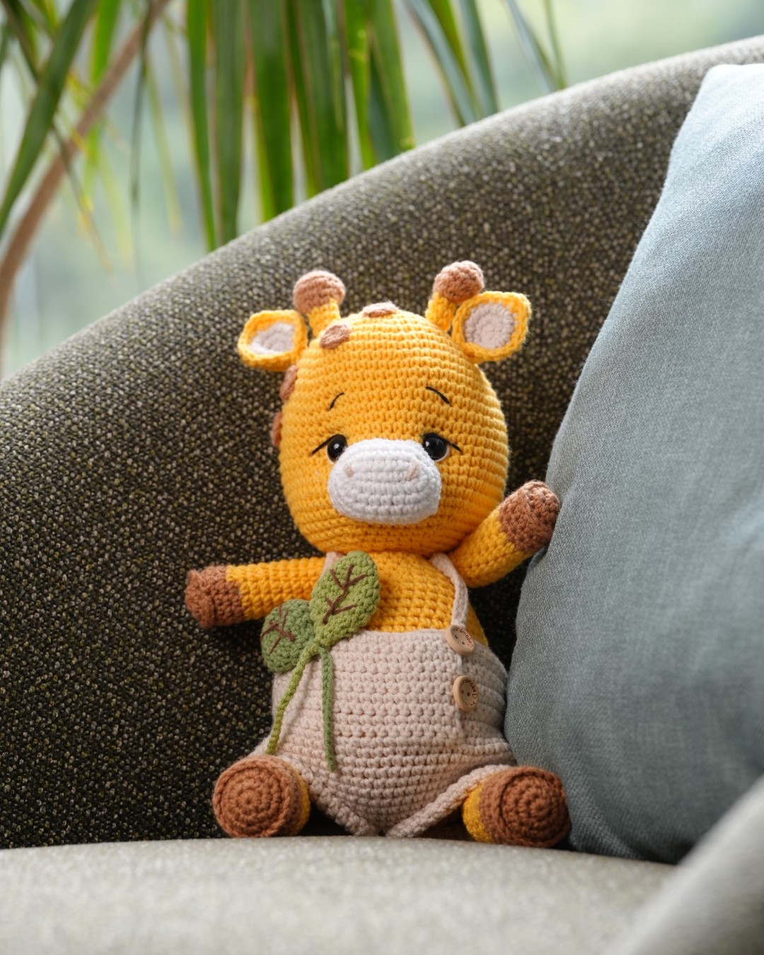 Handmade crochet Gigi the Giraffe in beige overalls on a chair